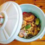 organic waste bin with lid. Food in the bin. Someone's hand opening the bin.