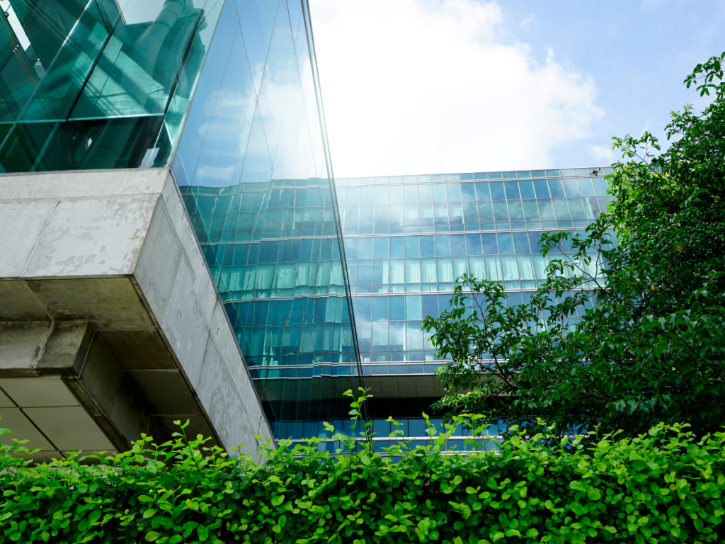 looking up at an office building with glass windows. bushes and trees surrounding